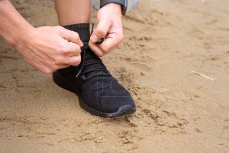 Photo for Man tie the lace on his shoes to start running and exercise. Runner tying running sneakers on the side walk or pavement of the road, getting ready to go for a run. Fitness, training and cardio - Royalty Free Image