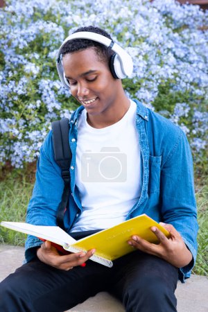 Foto de Un estudiante feliz con auriculares está dentro del campus universitario revisando el examen. Vida universitaria - Imagen libre de derechos