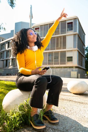 Photo for Young black woman wearing glasses, pointing thumbs up. Happy facial expression outdoors. - Royalty Free Image