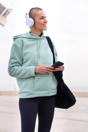 Téléchargez les photos : Une femme sportive avec casque fatiguée de l'exercice prend une pause pour utiliser une application de messagerie de téléphone portable à l'extérieur. - en image libre de droit