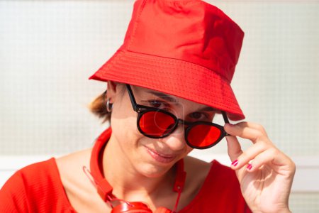 Téléchargez les photos : Élégante jeune femme souriante et regardant la caméra avec des lunettes et chapeau rouge.rait d'une belle femme caucasienne portant chapeau rouge et lunettes souriantes regardant la caméra. - en image libre de droit