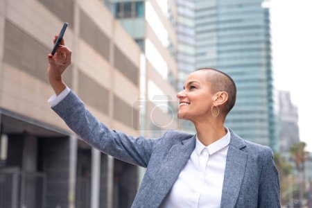 Foto de Hermosa mujer adulta caucásica feliz en traje sonriendo tomando una selfie al aire libre. - Imagen libre de derechos