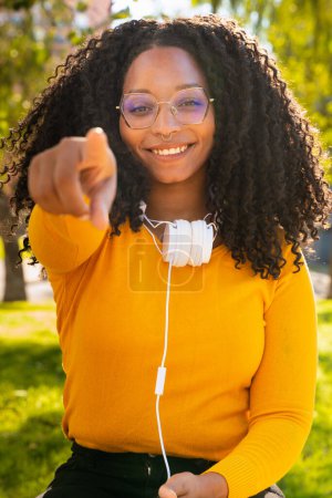 Photo for Young black woman wearing glasses, pointing thumb frontal, happy facial expression outdoors. - Royalty Free Image
