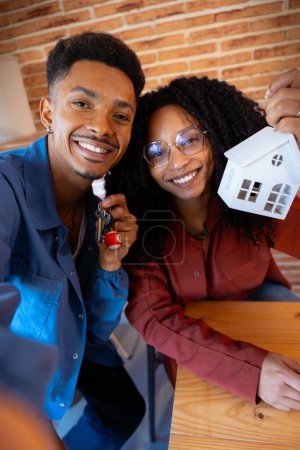 Téléchargez les photos : Homme et femme multiethnique avec mini maison et clés de leur nouvelle maison posant heureux en regardant la caméra. - en image libre de droit