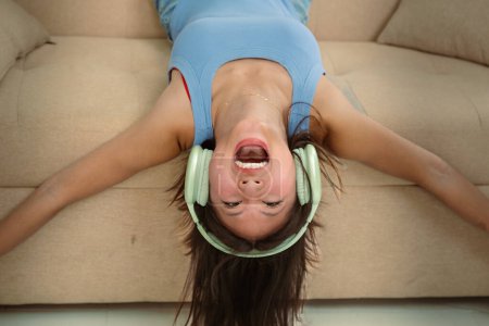 Photo for Happy woman, face down on the couch and headphones for music, audio streaming and well-being with fun at home. Podcast, radio playlist and online subscription, relax in the tech-enabled living room - Royalty Free Image