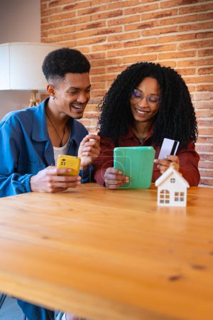 Photo for Multiracial Young Couple Sitting On Sofa Happy Entering Credit Card Number On Tablet To Make Easy And Secure Remote Electronic Payments - Royalty Free Image