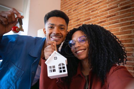 Foto de Hombre y mujer con mini casa y las llaves de su nueva casa posando feliz mirando a la cámara. - Imagen libre de derechos