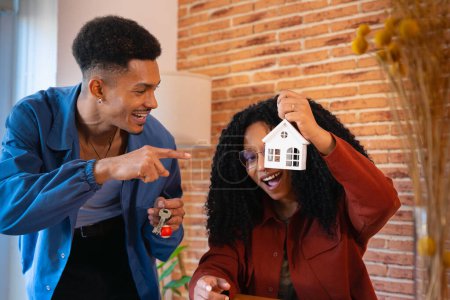 Foto de Hombre y mujer con mini casa y las llaves de su nueva casa posando feliz mirando a la cámara. - Imagen libre de derechos
