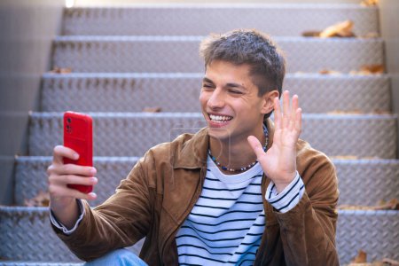 Téléchargez les photos : Un étudiant heureux est sur le campus universitaire pour faire un appel vidéo avec un téléphone mobile. Vie universitaire - en image libre de droit