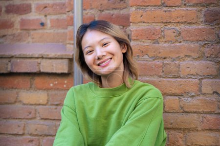 Téléchargez les photos : Belle adolescente chinoise riant en regardant la caméra à l'extérieur. Fille assise avec le visage heureux. - en image libre de droit