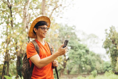 Téléchargez les photos : Portrait de jeune randonneur hispanique utilisant un téléphone portable profitant de la nature en forêt. - en image libre de droit