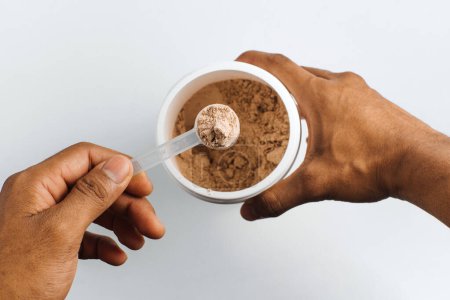 Photo for Hands holding a scoop of chocolate protein over white background. - Royalty Free Image
