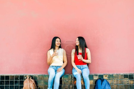 Photo for Two happy and cheerful Latin American girl friends sitting while talking. urban concept and student life - Royalty Free Image