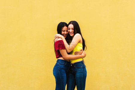 Foto de Dos jóvenes amigos latinoamericanos abrazándose en la pared amarilla. - Imagen libre de derechos