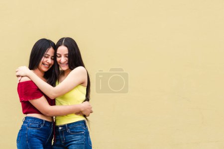 Photo for Two young latin americans friends hugging on yellow wall outdoors, happiness and friendship concept. - Royalty Free Image