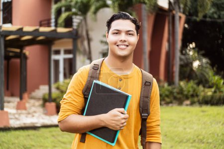 Téléchargez les photos : Jeune étudiant hispanique souriant heureux portant un sac à dos sur le campus universitaire. - en image libre de droit