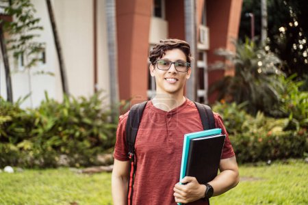 Téléchargez les photos : Jeune étudiant hispanique souriant heureux portant un sac à dos sur le campus universitaire. - en image libre de droit