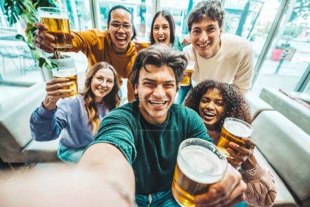 Foto de Grupo de personas multirraciales disfrutando de la hora feliz bebiendo cerveza sentados en la mesa del bar. Concepto de estilo de vida con chicos y chicas pasando el rato - Imagen libre de derechos