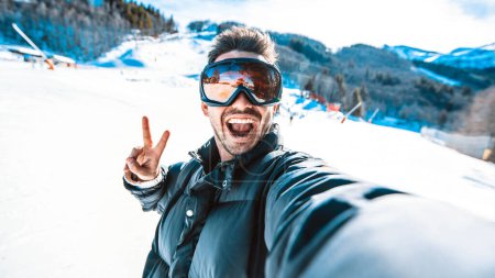 Foto de Guapo esquiador divertido está tomando una selfie en invierno en la nieve en una montaña - Foto de alta calidad - Imagen libre de derechos