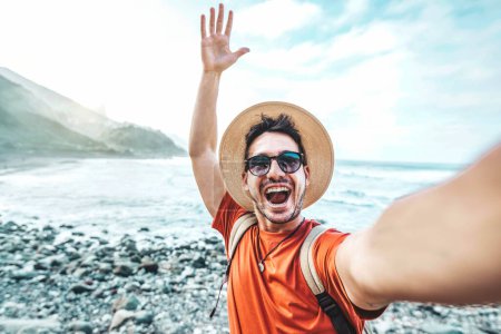 Foto de Hombre guapo feliz tomando foto selfie con dispositivo de teléfono móvil inteligente fuera - Blogger de viajes en streaming en vivo en la plataforma social - Turismo, viajes, personas y concepto de tecnología - Imagen libre de derechos