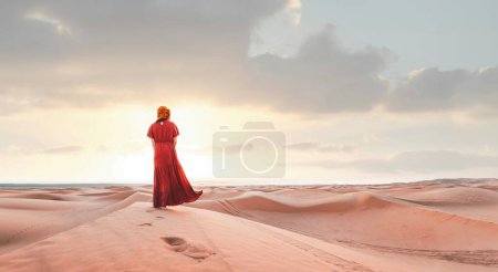 Woman wearing hijab walking in the desert sand dunes at sunset -Wanderlust, wellbeing, happiness and traveling concept