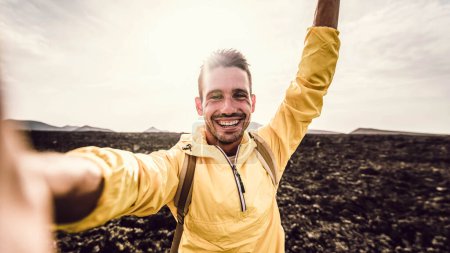 Téléchargez les photos : Un bel homme qui grimpe un rocher en selfie. Randonneur souriant prenant un portrait avec action cam randonnée une montagne au coucher du soleil - en image libre de droit