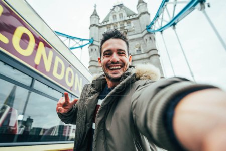Photo for Smiling man taking selfie portrait during travel in London, England - Young tourist male taking memory pic with iconic england landmark - Happy people wandering around Europe concept - Royalty Free Image