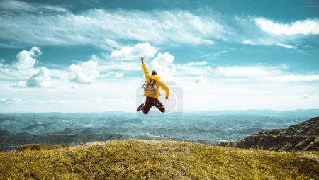 Foto de Caminante con mochila levantando las manos saltando en la cima de una montaña - Hombre exitoso con los brazos arriba disfrutando de la victoria - Concepto de deporte y éxito - Imagen libre de derechos