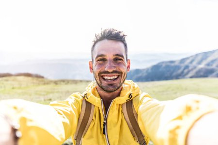 Téléchargez les photos : Happy hiker guy taking a selfie on the top of a mountain - Souriant homme regardant caméra - Beau visage masculin en plein air - en image libre de droit
