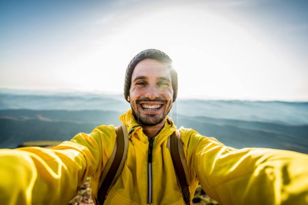 Foto de Chico excursionista feliz tomando una selfie en la cima de una montaña - Hombre sonriente mirando cámara - Hombre guapo cara al aire libre - Imagen libre de derechos