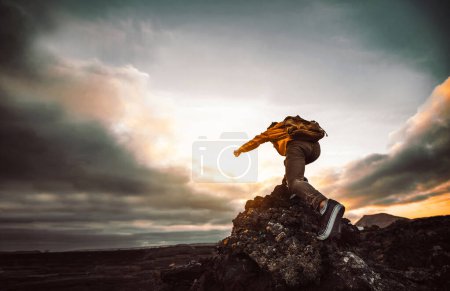 Foto de Caminante de pie en la montaña del acantilado señalando el cielo con los dedos al atardecer - Hombre en acantilado rocoso mirando hacia abajo al paisaje - Concéntrate en el zapato - Imagen libre de derechos
