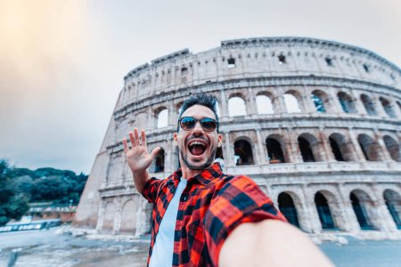 Happy tourist visiting Colosseum in Rome, Italy - Young man taking selfie in front of famous Italian landmark - Travel and holidays concept