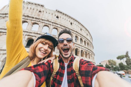 Happy couple visiting Colosseum in Rome, Italy. Young Friends takes selfie with smart phone at Coliseum - Guy and Girl visiting together Europe - travel influencer tecnology and love concept