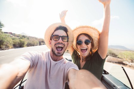 Foto de Feliz hermosa pareja enamorada de tomar un retrato selfie conducir un coche convertible en la carretera en las vacaciones. Alquiler de coches, vacaciones y personas - Imagen libre de derechos