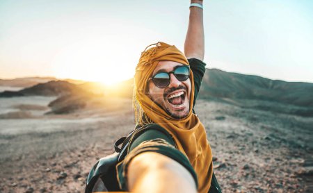 Photo for Handsome toyrist man taking selfie with smart mobile phone outside at golden hour time - Happy guy with backpack enjoying day out - Royalty Free Image