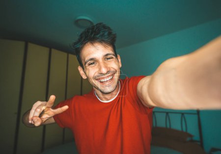 Téléchargez les photos : Jeune homme prenant selfie à la maison - Photo de beau gars dans le salon profiter week-end - Homme habillé occasionnel en appel vidéo riant à la caméra - en image libre de droit