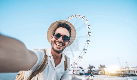 Photo for Happy tourist taking selfie on summer vacation - Smiling guy looking at camera outside - Millenial taking photo with smart mobile phone - Focus on eye - Royalty Free Image