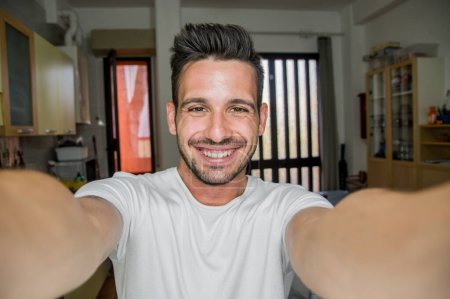 Téléchargez les photos : Bel homme caucasien prenant un portrait selfie à l'intérieur à la maison - gars heureux souriant à la caméra - concept Lifestye - en image libre de droit