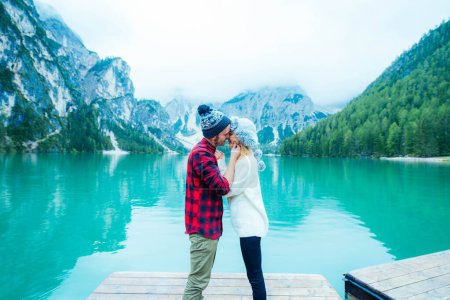 Téléchargez les photos : Couple de touristes visitant un lac alpin à Braies, Italie. Petit ami et petite amie s'embrassant sur une jetée sur un fond de luxure - Filtre vintage bleu. - en image libre de droit