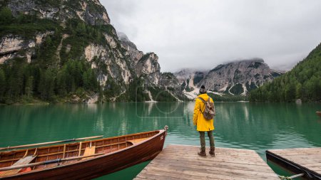 Téléchargez les photos : Vue arrière portrait d'un randonneur visitant un lac alpin à Braies, Italie. Homme heureux vêtu d'une veste jaune et sac à dos profiter du paysage naturel à l'automne. Désir et voyage. - en image libre de droit