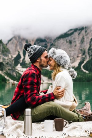 Photo for Romantic kiss of a couple of adults visiting an alpine lake at Braies Italy. Tourist in love spending loving moments together at autumn fall. Couple, wanderlust and travel concept. - Royalty Free Image