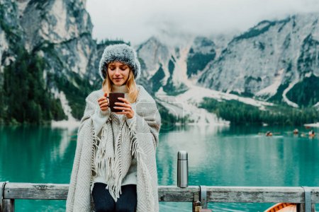 Téléchargez les photos : Portrait d'une belle jeune femme buvant du café chaud visitant un lac alpin à Braies Italie. Touriste féminine profitant de moments de détente à la montagne. Les gens, l'errance et les voyages. - en image libre de droit