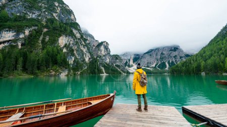 Foto de Retrato retrovisor de un excursionista que visita el lago alpino en Braies, Italia. Hombre feliz con chaqueta amarilla y mochila disfrutar del paisaje de la naturaleza en otoño. Wanderlust y viajes. - Imagen libre de derechos