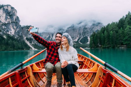 Téléchargez les photos : Couple romantique d'adultes amoureux prenant un selfie sur un bateau visitant un lac alpin à Braies Italie à l'automne. - en image libre de droit