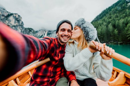 Téléchargez les photos : Couple romantique d'adultes amoureux prenant selfie sur un bateau visitant un lac alpin à Braies, Italie - Couple, technologie, voyage et concept de mode de vie heureux - Couleurs froides. - en image libre de droit