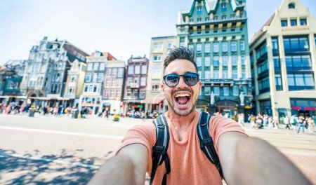 Happy tourist taking selfie picture in Amsterdam, Netherlands - Homme joyeux utilisant un appareil de téléphonie mobile intelligent à l'extérieur - Voyageur étudiant profitant de vacances d'été en Europe - Concept de tourisme de style de vie