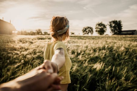 Foto de Retrato de una joven feliz cogida de la mano de su novio mientras caminaba por un campo de trigo al atardecer. Pareja disfrutando de los viajes en la naturaleza - Imagen libre de derechos