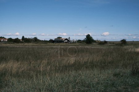 Photo for Nestled in the Danish countryside, a traditional house stands amidst a vast field, offering a glimpse into the serene rural life against a backdrop of clear skies and natural landscapes. - Royalty Free Image