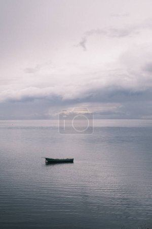 Photo for A solitary boat floats on the calm waters of Denmark, under a moody sky at dusk, creating a serene and contemplative scene that captures the essence of solitude and the beauty of Scandinavian evenings. - Royalty Free Image