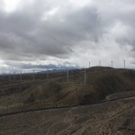 Wind turbines stand sentinel on the desert hills, their blades turning steadily as they harness the power of the wind, a symbol of renewable energy captured by the expansive eye of a drone.